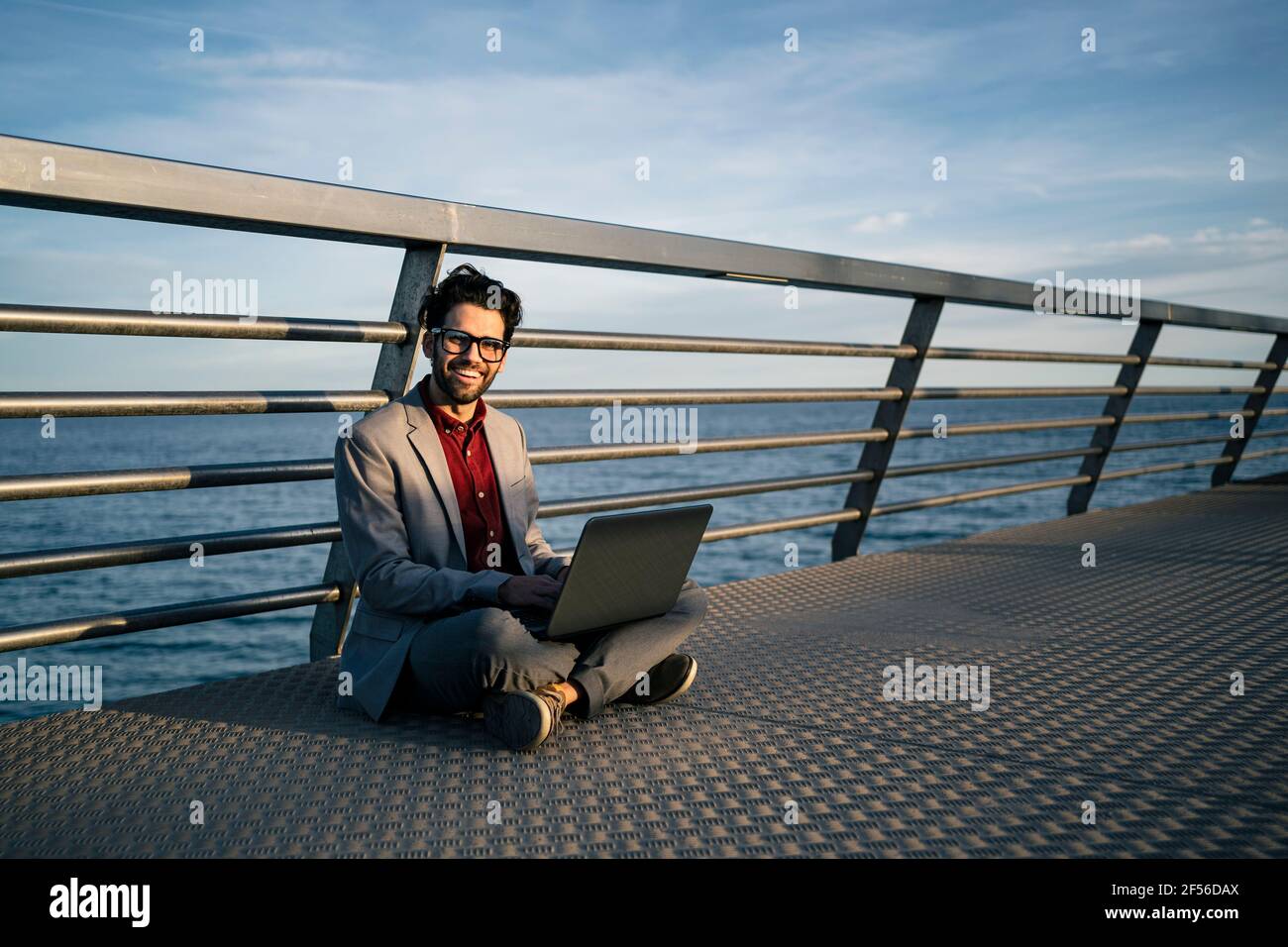 Travailleur indépendant souriant avec un ordinateur portable assis à pieds croisés sur la jetée Banque D'Images