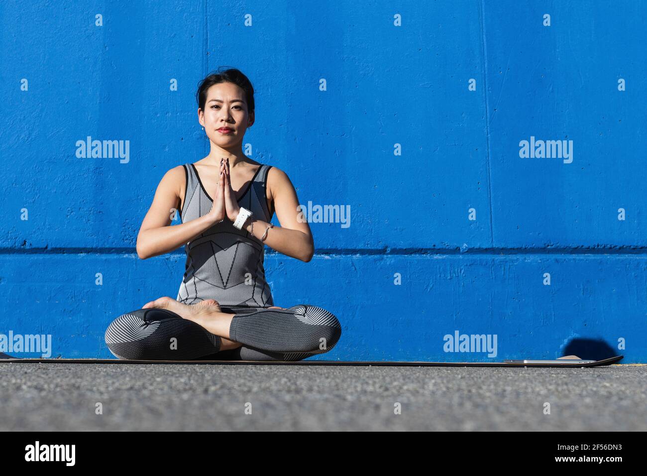 Belle femme avec les mains clasped faisant du yoga contre le mur bleu Banque D'Images