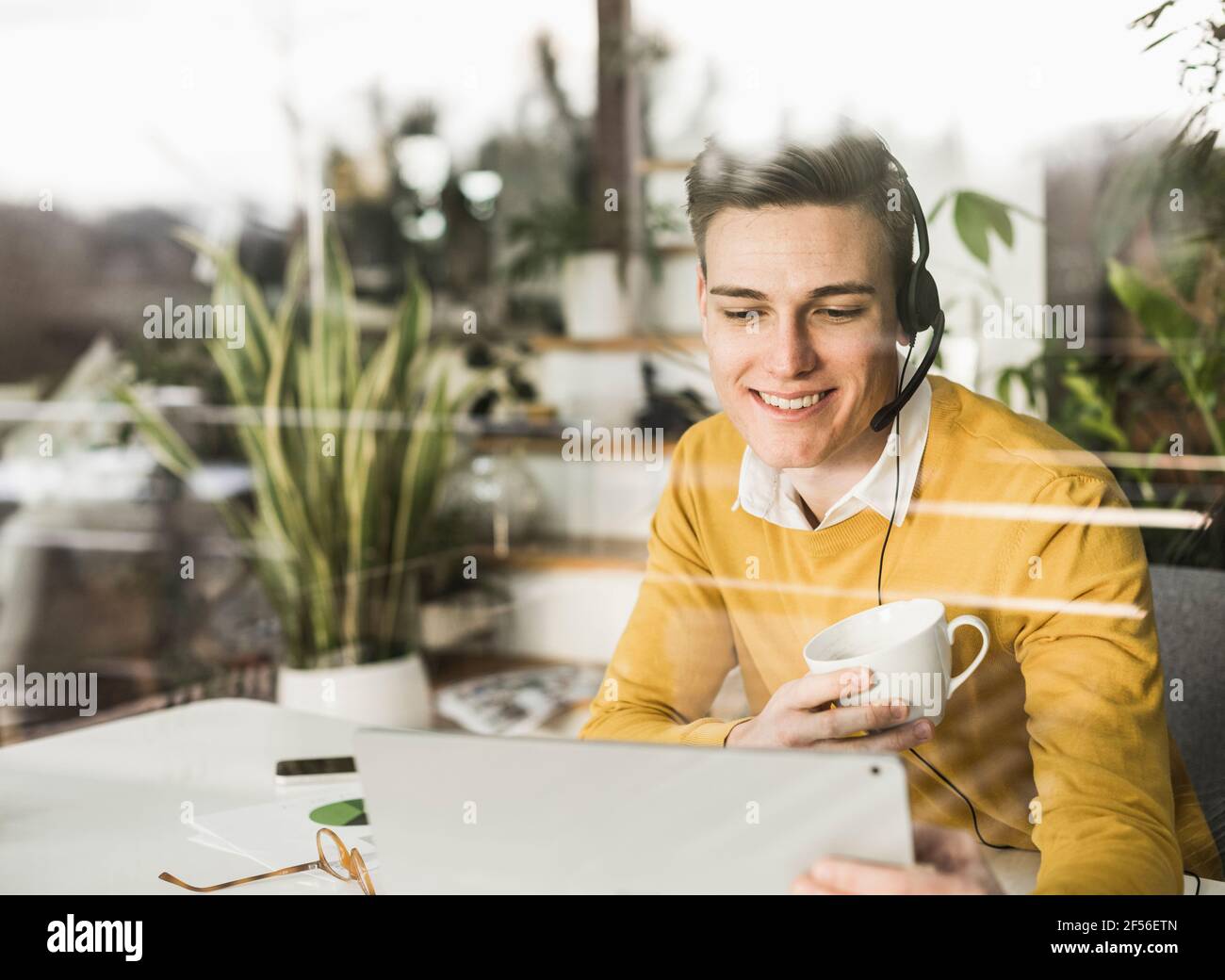 Un jeune homme d'affaires vu par la fenêtre pendant qu'il travaille au bureau à domicile Banque D'Images
