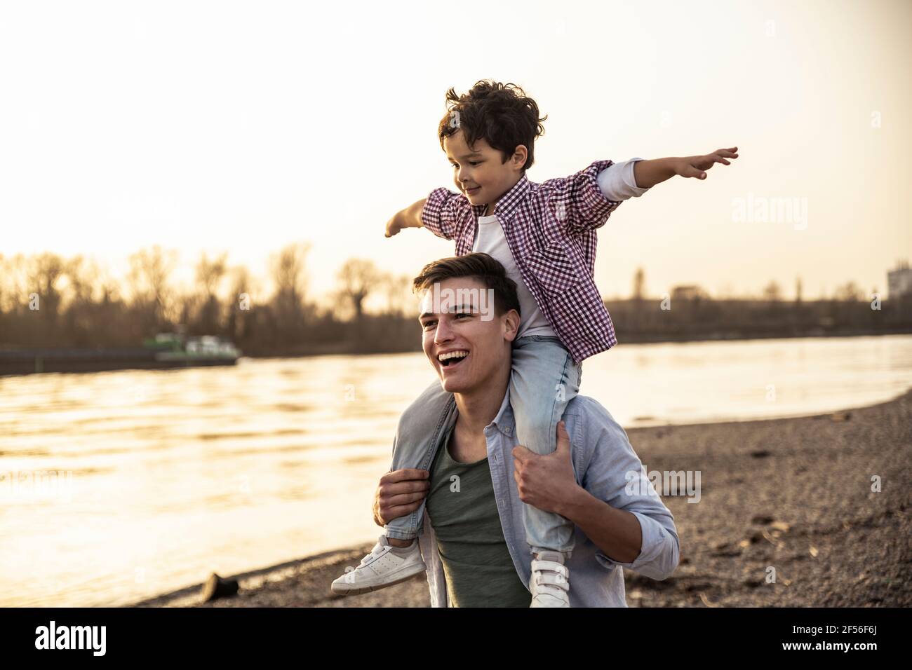 Homme souriant garçon joueur sur les épaules au bord du lac Banque D'Images