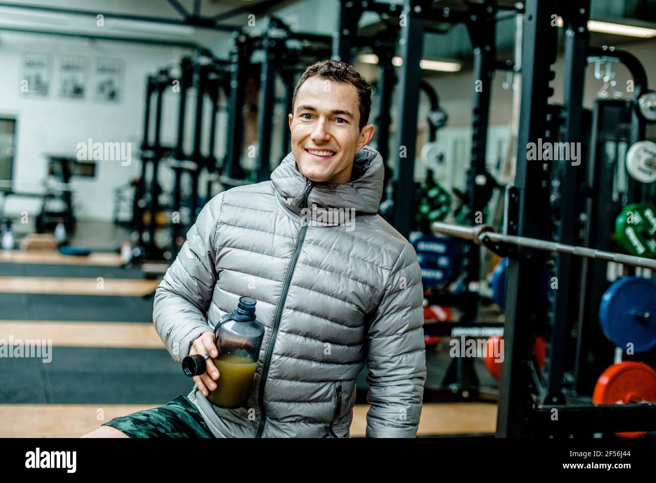 Homme souriant dans une veste matelassée ayant une boisson énergétique à la salle de gym Banque D'Images