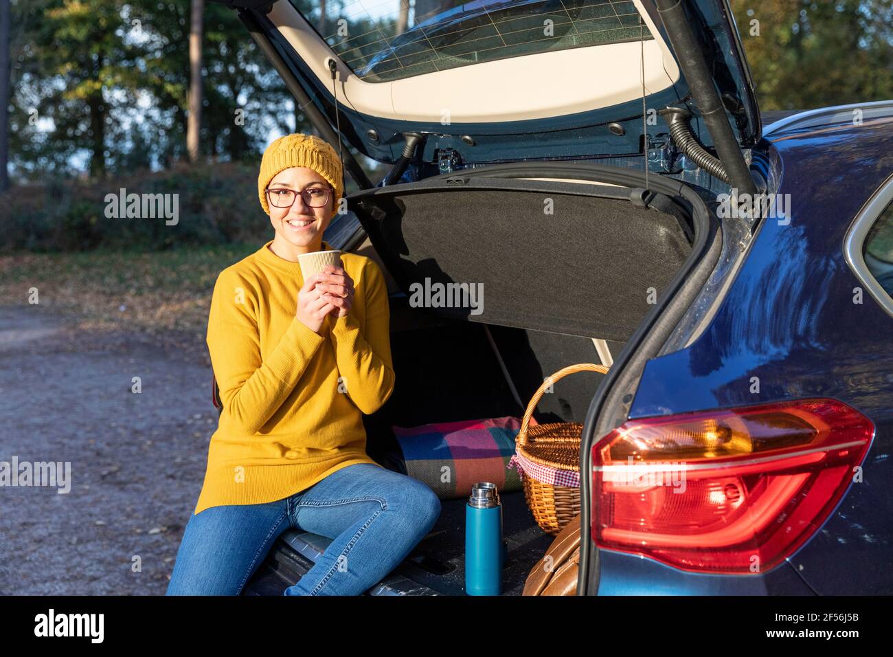 Femme souriante prenant une boisson chaude dans le coffre de la voiture Banque D'Images