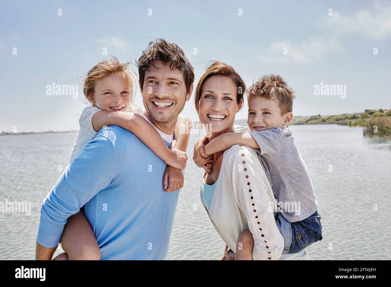 Des parents souriants qui dorment les enfants au bord du lac par beau temps Banque D'Images