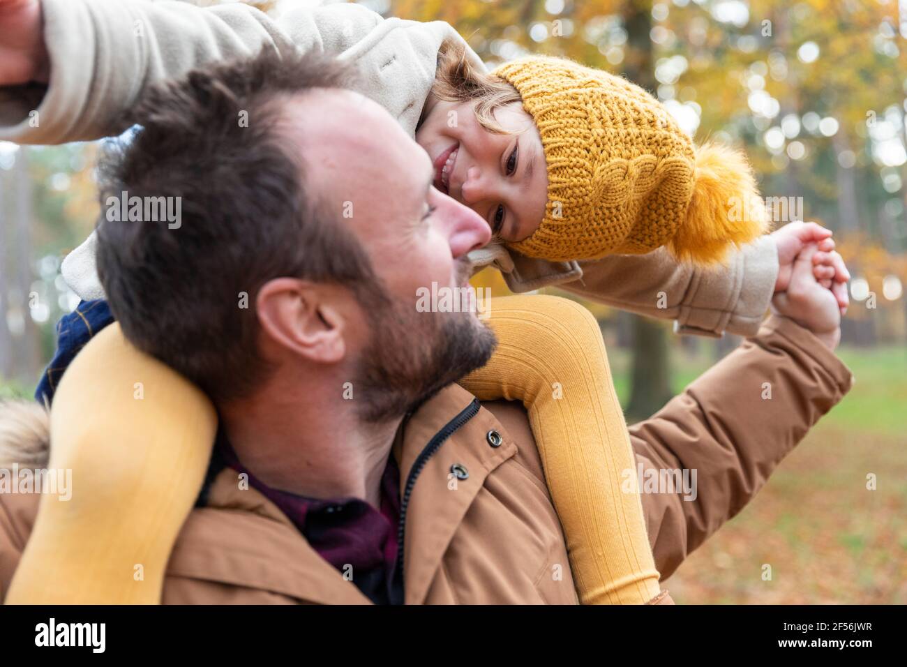 Fille souriante jouant tout en étant assise sur l'épaule du père dans la forêt Banque D'Images