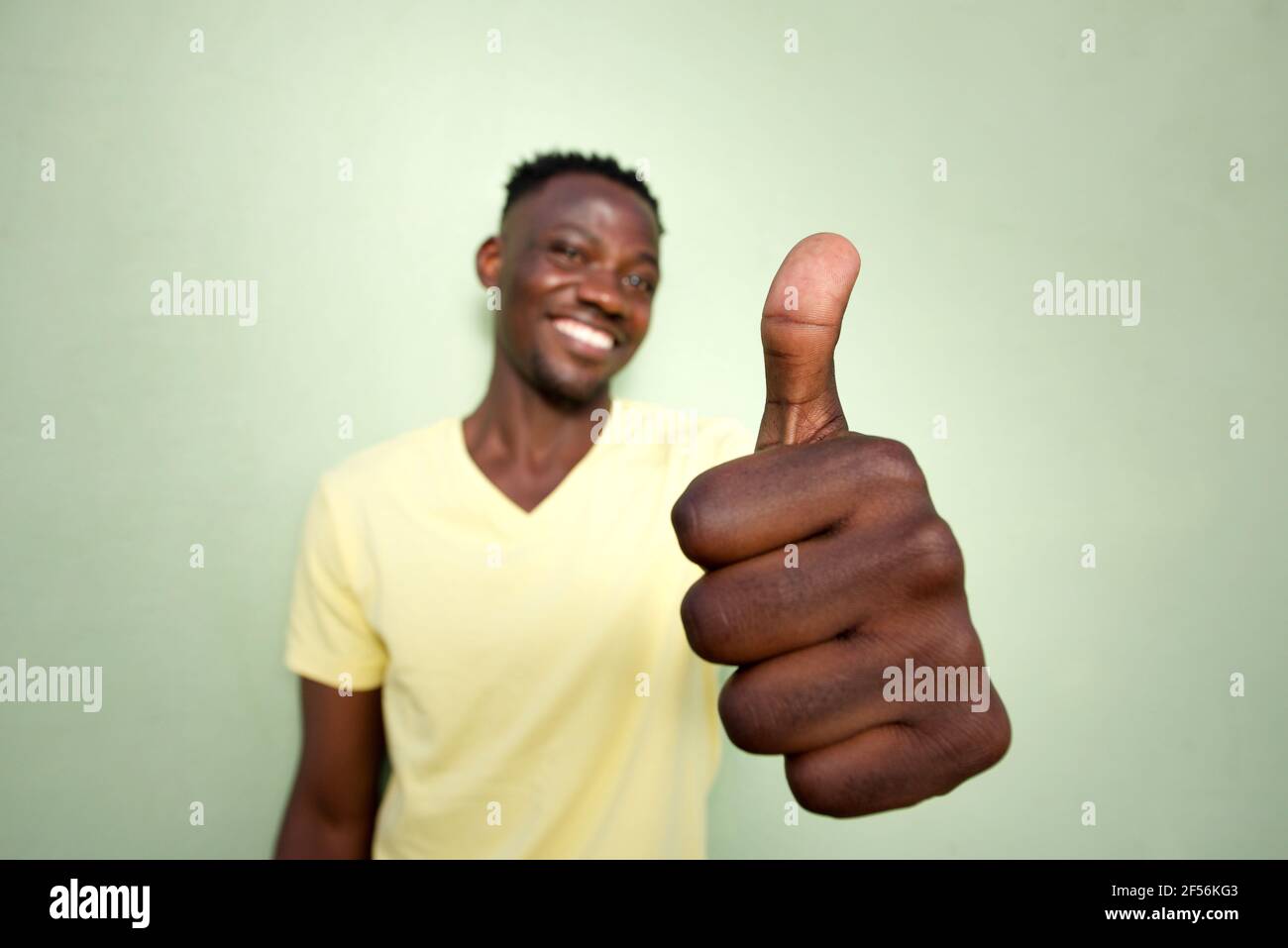 Portrait grand angle de jeune homme noir qui fait des gestes avec le pouce vers le haut signe par le mur vert Banque D'Images