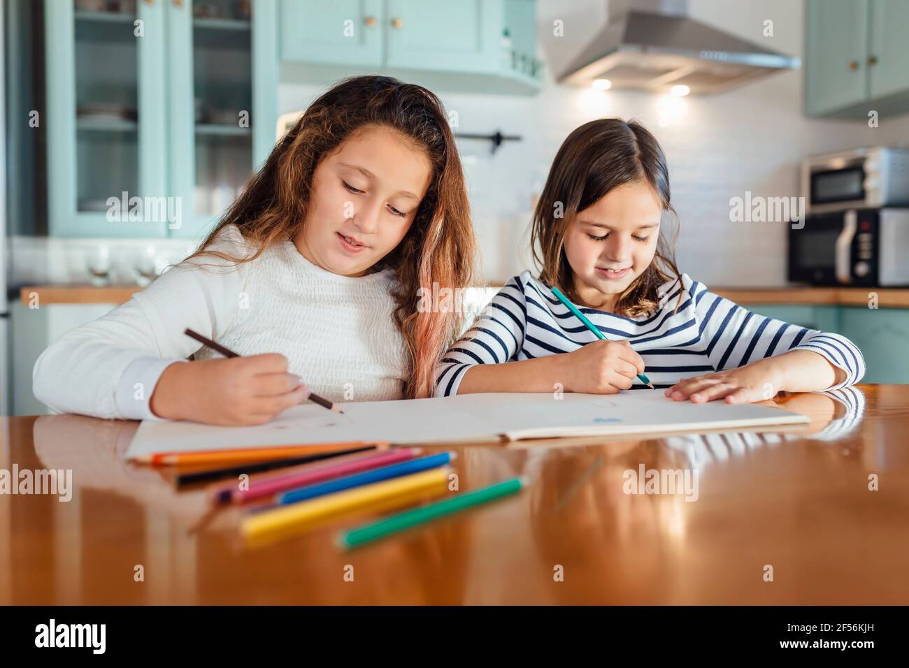 Les sœurs se colorent avec un crayon de couleur sur papier tout en étant assis table à manger dans la cuisine Banque D'Images