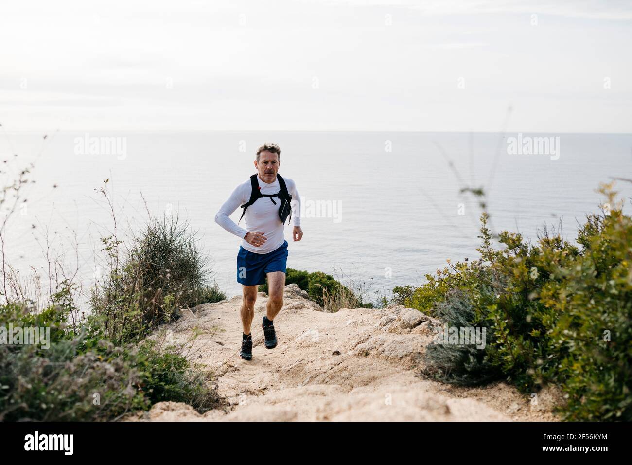 Homme qui court en montagne près de la mer contre un ciel nuageux Banque D'Images