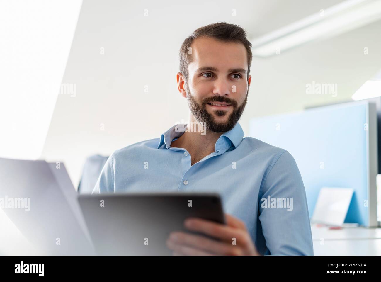 Homme d'affaires avec papier et tablette numérique souriant au bureau Banque D'Images