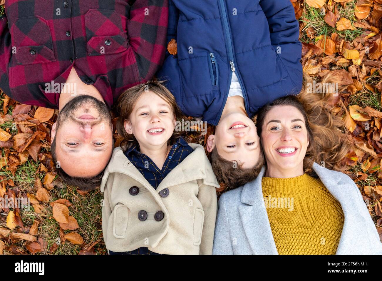 Famille souriant tout en se reposant sur la feuille tombée dans la forêt pendant automne Banque D'Images