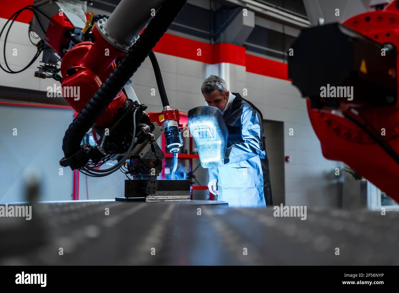 Soudeur avec casque de soudage examinant la robotique en usine Banque D'Images