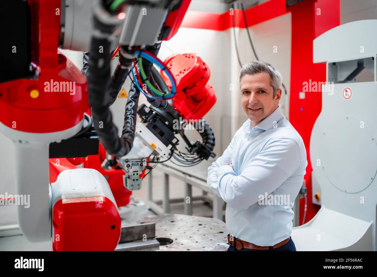 Un ingénieur souriant aux bras croisés debout à l'usine de robotique Banque D'Images