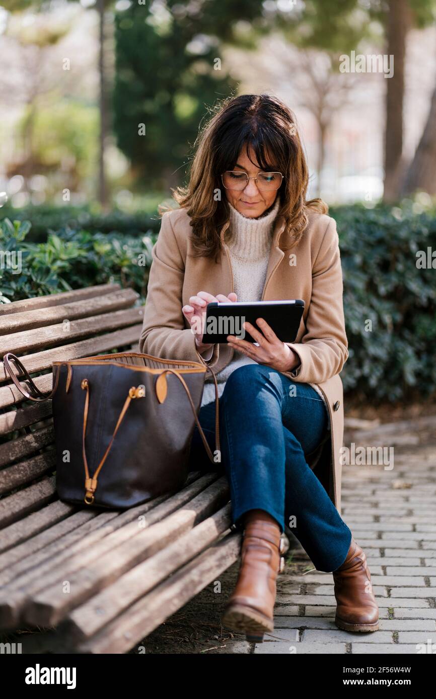 Femme mature utilisant une tablette numérique assis sur un banc stationnement Banque D'Images