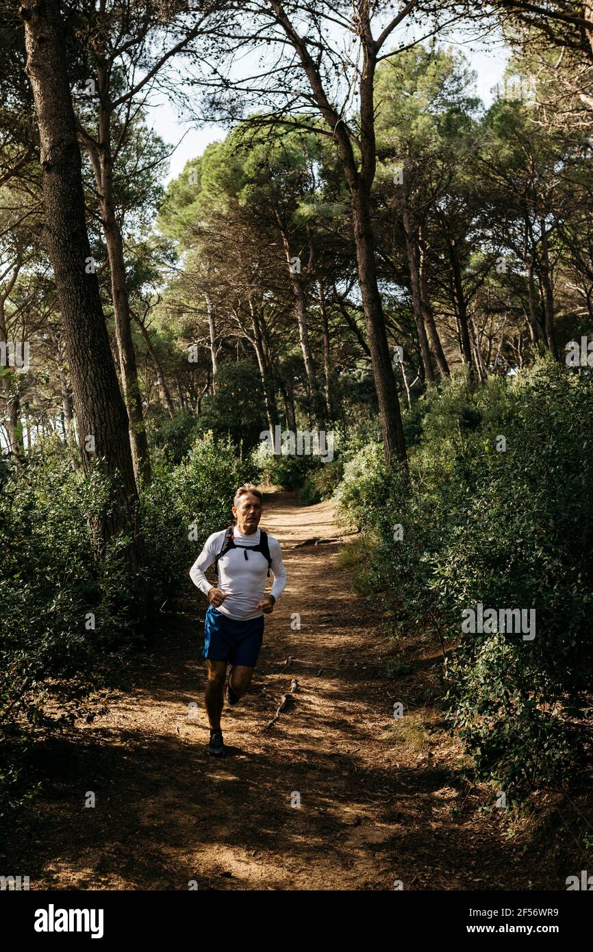 Homme en train de courir sur la route de terre dans la forêt Banque D'Images