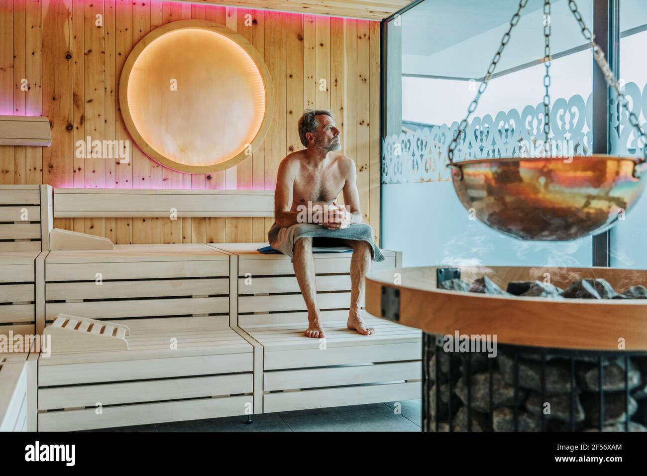 Homme regardant par la fenêtre tout en s'asseyant au sauna finlandais Banque D'Images