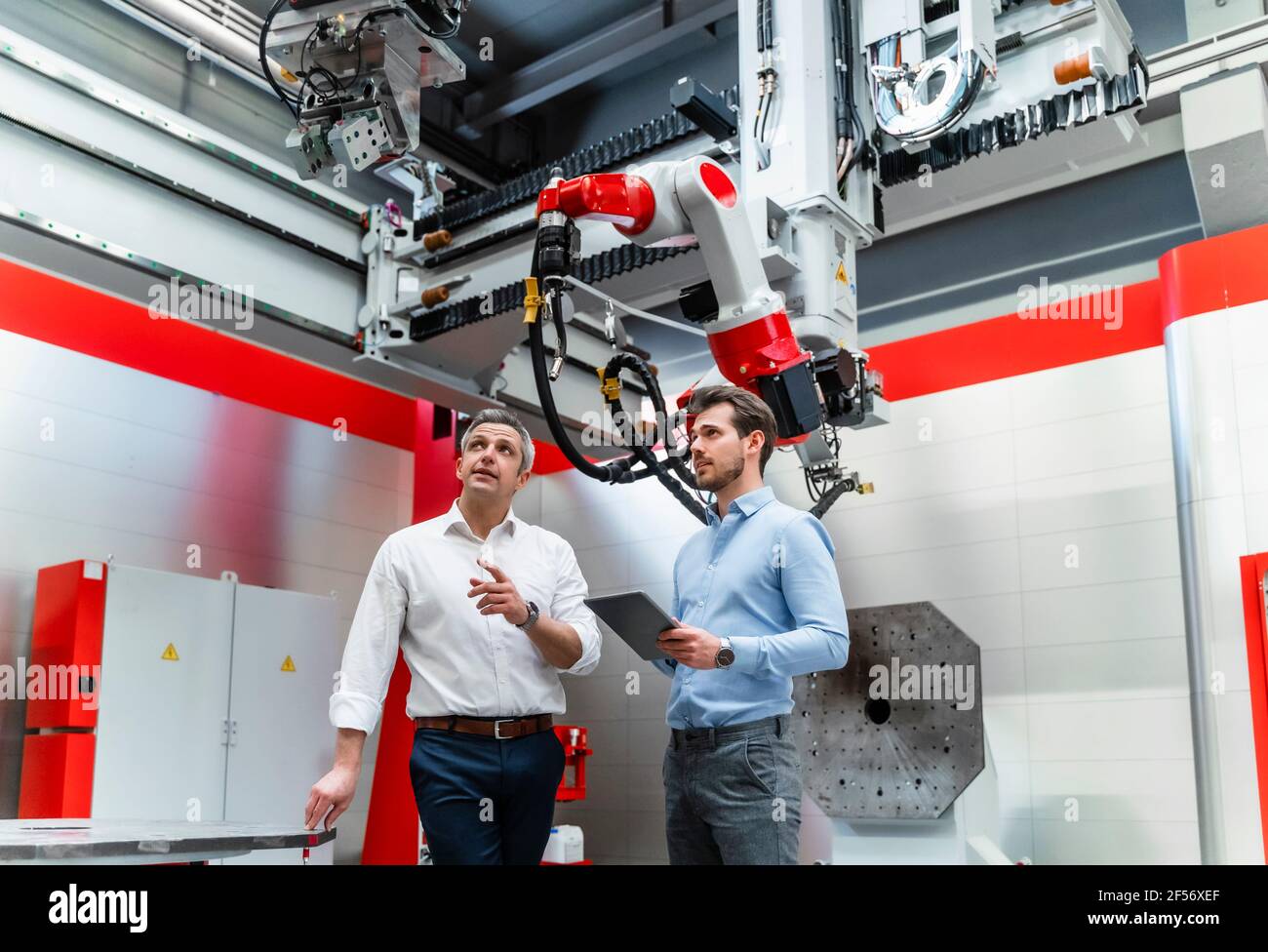 Ingénieur en automatisation mature expliquant le robotique au jeune homme avec le numérique tablette en usine Banque D'Images
