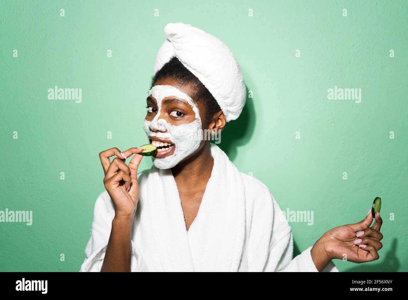 Femme avec masque facial mangeant le concombre tout en se tenant contre le vert arrière-plan Banque D'Images