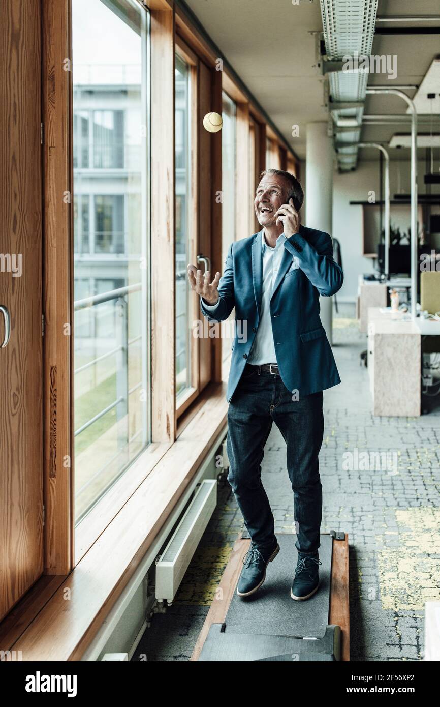 Joyeux homme d'affaires en train de faire des gestes tout en parlant à travers le téléphone mobile sur un tapis roulant au bureau Banque D'Images