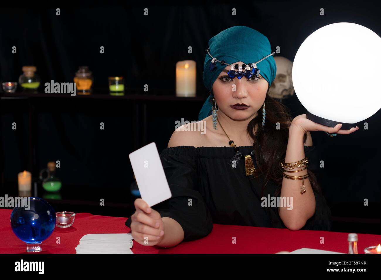 Belle fortune-teller dans une robe noire tenant une boule de cristal blanc et des cartes de tarot utilisées pour prédire les fortunes. Banque D'Images