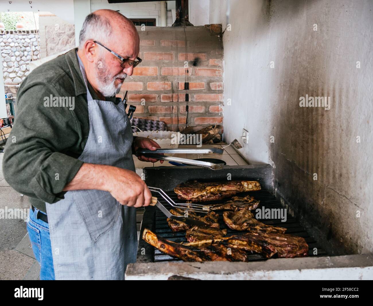 OL man cuisant le steak de bœuf grillé Tomahawk sur un gril noir chaud Banque D'Images