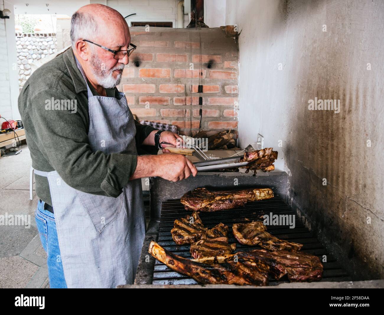 OL man cuisant le steak de bœuf grillé Tomahawk sur un gril noir chaud Banque D'Images