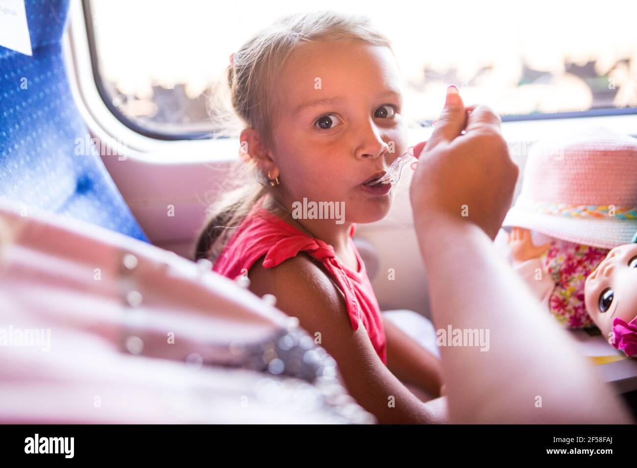 La main de mère nourrit la petite fille avec du yaourt pendant le trajet de 500 km en train de Kiev à Dnepr en Ukraine. La jeune dame aime le voyage assis par la fenêtre Banque D'Images