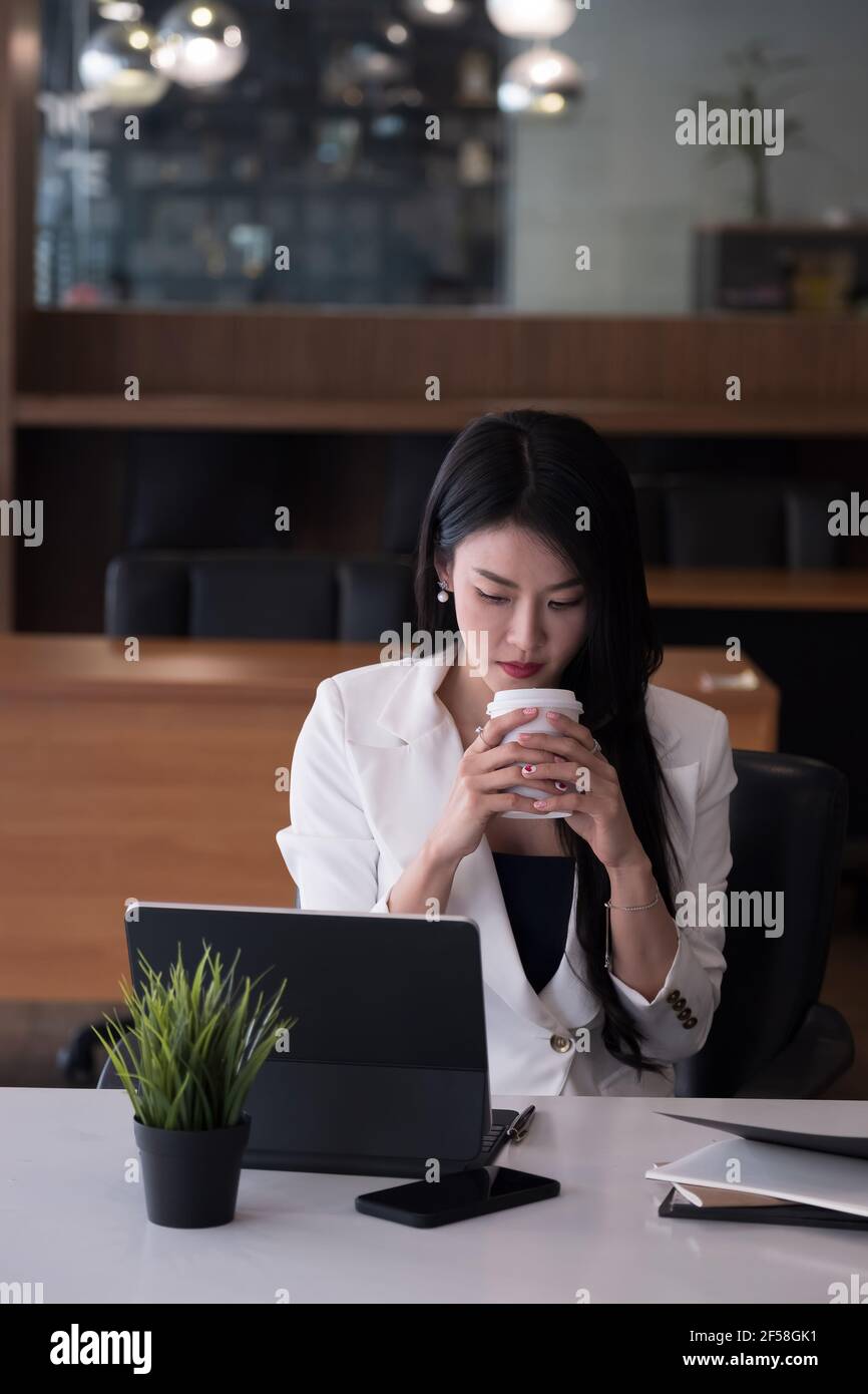 Portrait d'entreprise ou comptable assis à un bureau dans un cadre moderne bureau avec boissons chaudes à l'intérieur tenant une tasse dans les mains pendant la visioconférence Banque D'Images