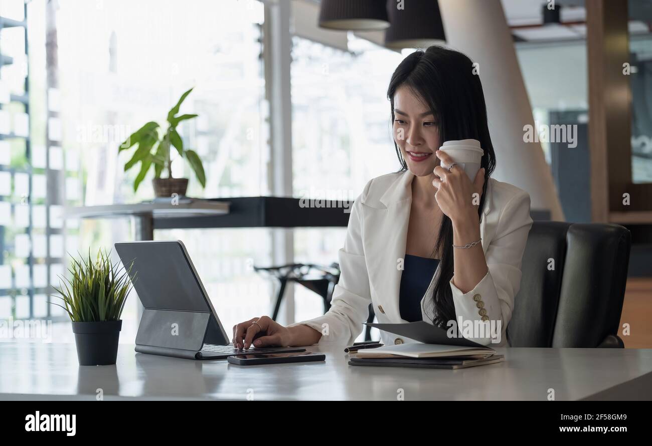 Portrait d'entreprise ou comptable assis à un bureau dans un cadre moderne bureau avec boissons chaudes à l'intérieur tenant une tasse dans les mains pendant la visioconférence Banque D'Images