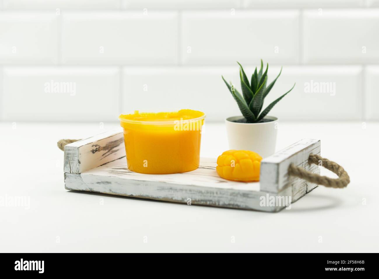 Un savon de mangue jaune fait à la main, un gommage à la mangue et un potté vert succulent stand sur un plateau en bois dans une salle de bains moderne Banque D'Images