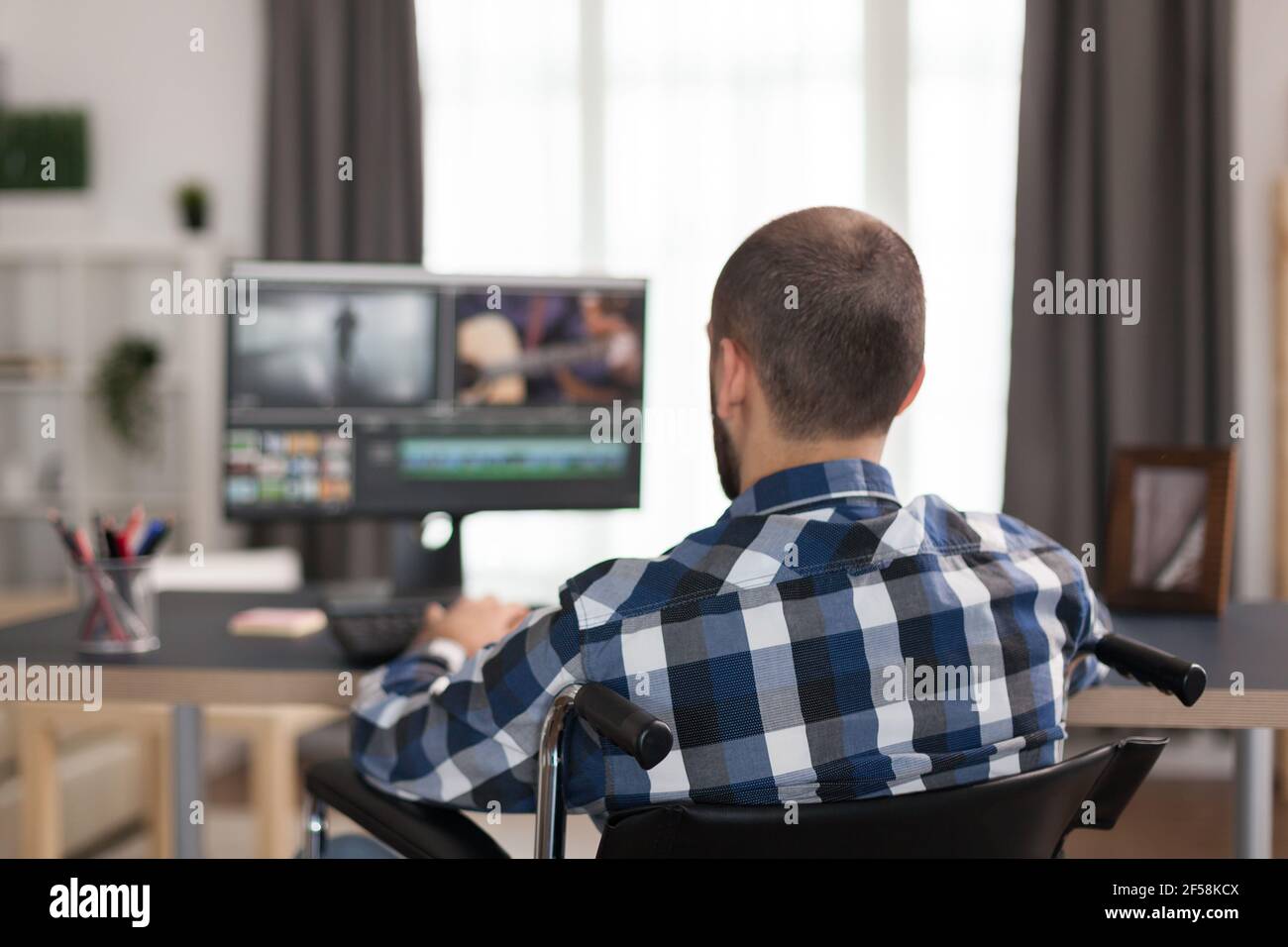 Un réalisateur handicapé travaillant en fauteuil roulant en post-production de films. Un vidéaste non valide faisant ses affaires en ligne, utilisant la haute technologie, assis dans son appartement, travaillant à distance dans des conditions spéciales. Banque D'Images