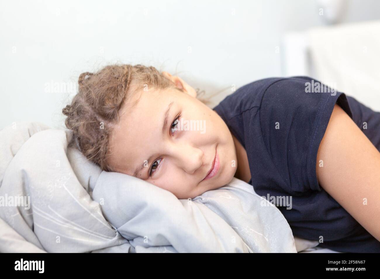 Belle jeune fille couchée avec un oreiller confortable sur un lit, regardant l'appareil photo Banque D'Images