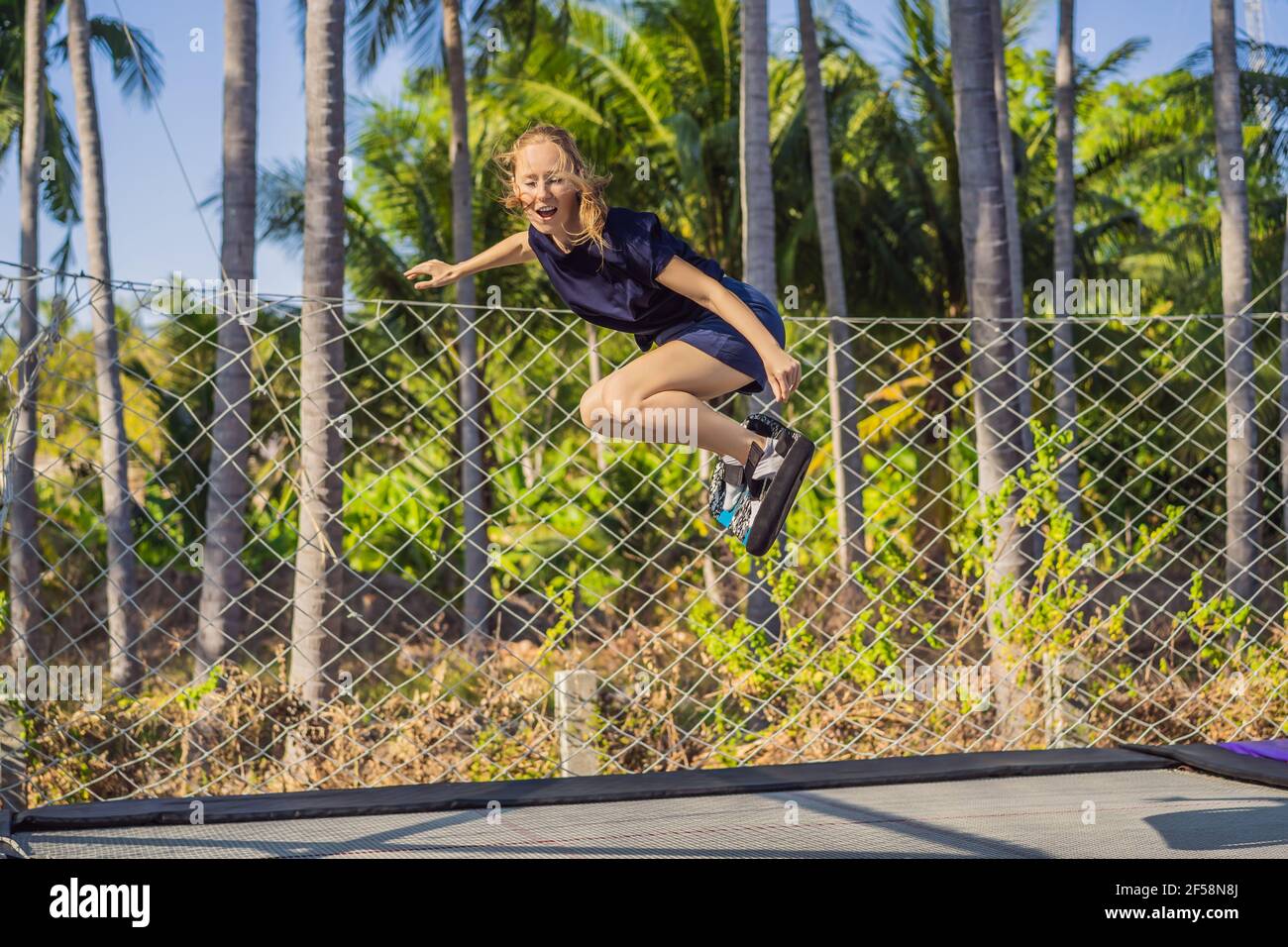 Jeune femme sur un plateau souple pour un trampoline sautant sur un  trampoline extérieur, sur fond de palmiers. Le trampoline est comme un  Photo Stock - Alamy