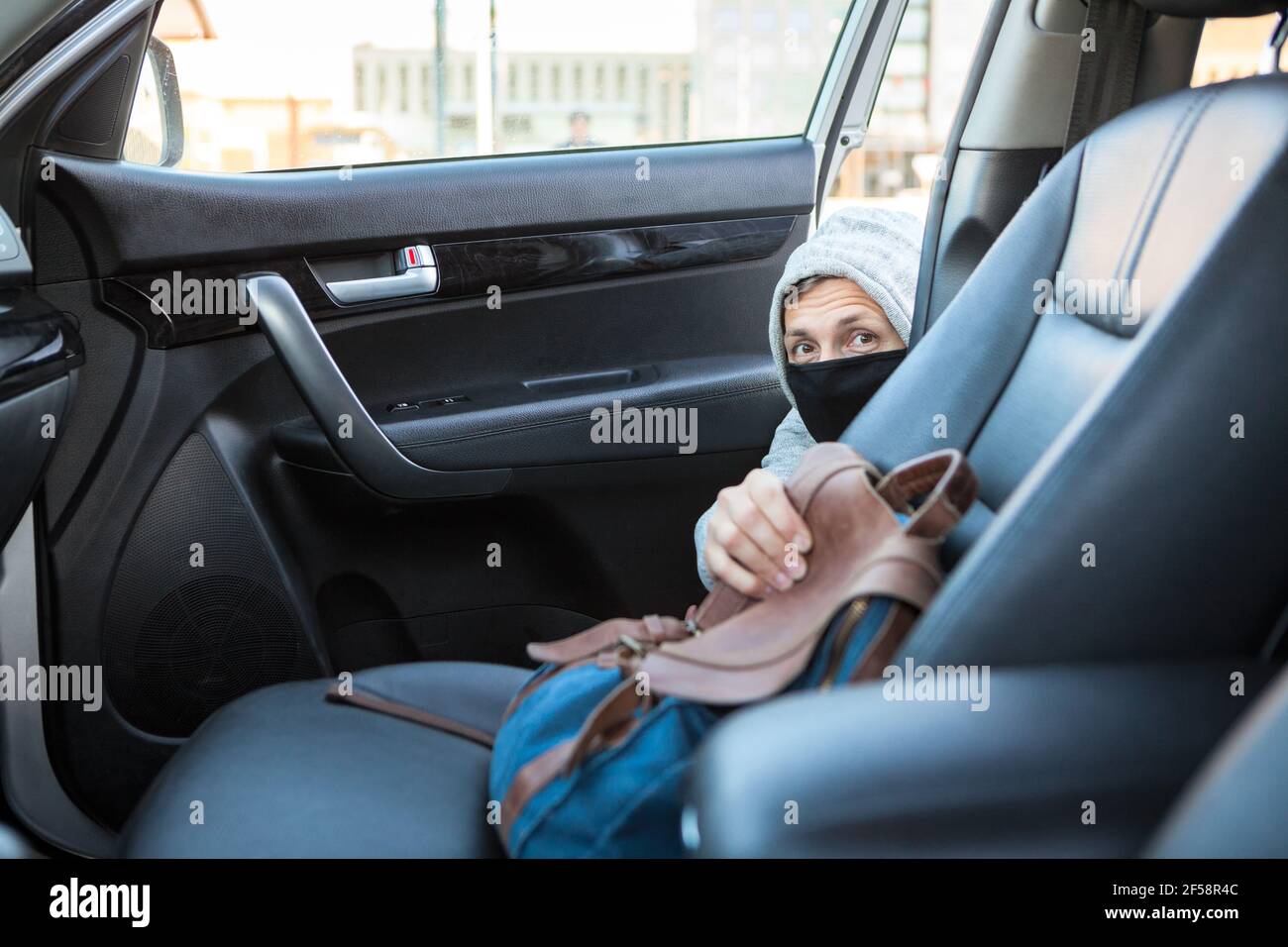 Vol de sac d'une voiture, homme méconnaissable dans un masque noir et un  sweat à capuche emportant un sac à main femelle du siège passager avant  Photo Stock - Alamy