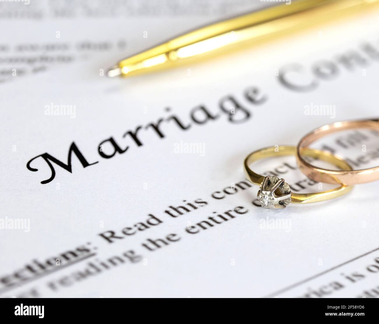 Contrat de mariage avec deux anneaux de mariage d'or et stylo d'or, accord prénuptial, macro gros plan, signer avec la signature, document, concept d'accord Banque D'Images