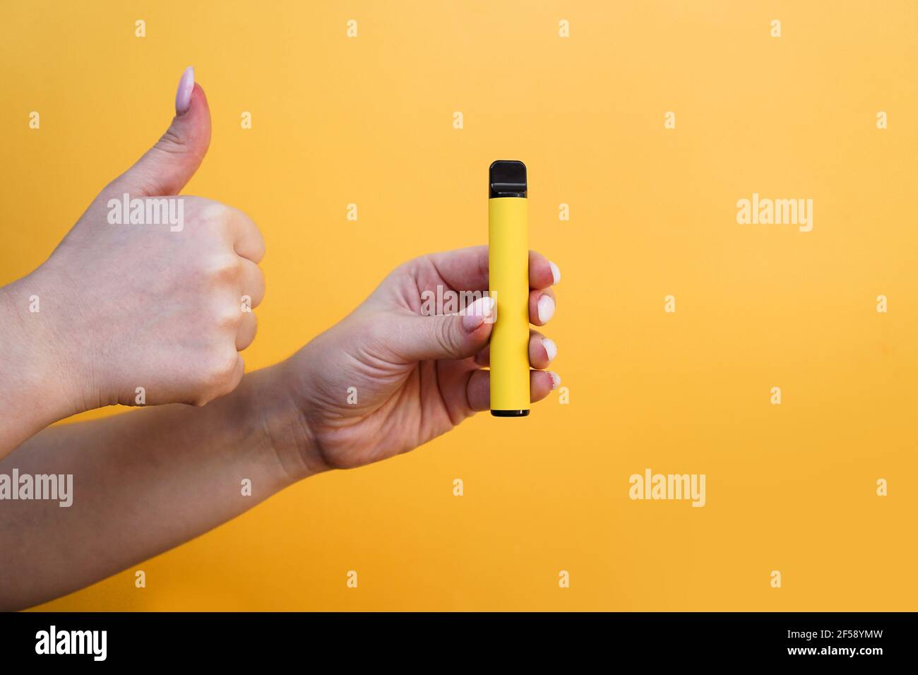 Cigarette électronique jaune jetable dans la main femelle. La main montre  les pouces vers le haut Photo Stock
