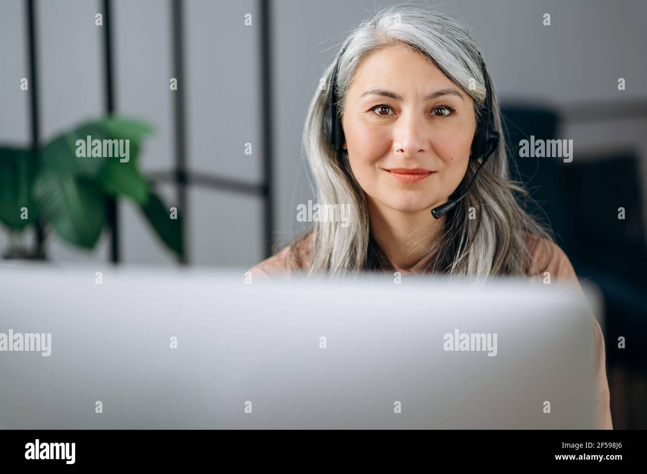 Portrait de belle femme asiatique, femme d'affaires, avocate, agent immobilier, avec un casque devant l'ordinateur, regardant l'appareil photo, souriant sympathique Banque D'Images