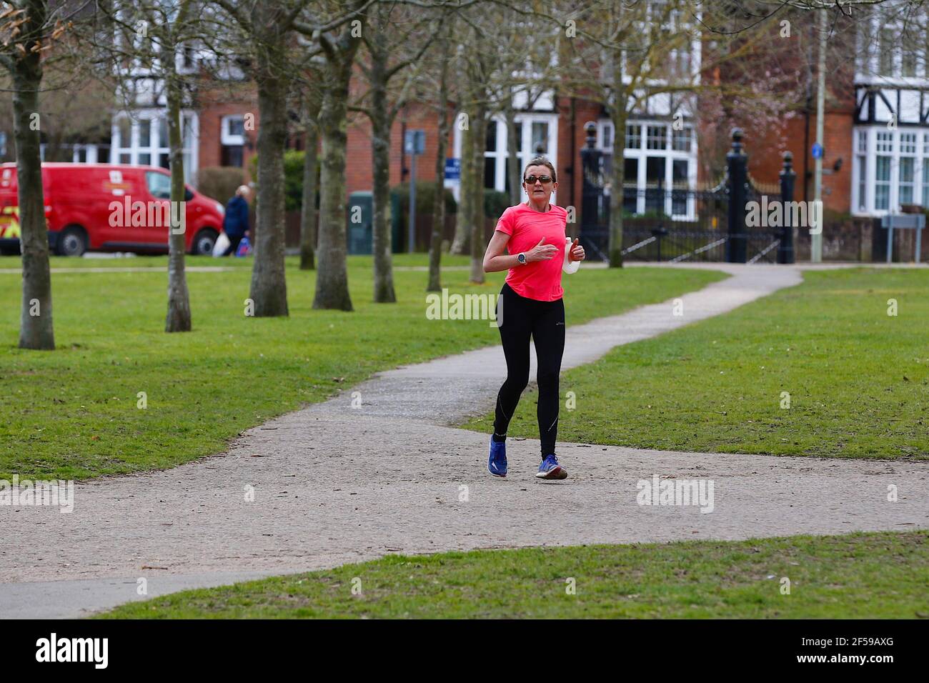 Ashford, Kent, Royaume-Uni. 25 mars 2021. Météo au Royaume-Uni : les gens apprécient le parc Victoria à Ashford, dans le Kent, tandis que les intervalles ensoleillés offrent un agréable soleil de printemps chaud. Un jogging dans un haut lumineux court autour du parc Victoria. Crédit photo : Paul Lawrenson /Alay Live News Banque D'Images