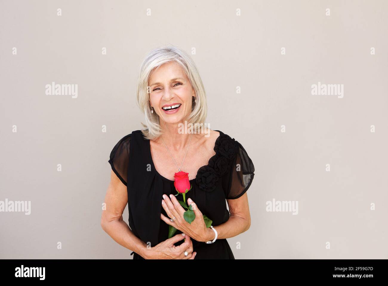 Portrait d'une belle femme âgée en train de rire avec une rose rouge blouse noire Banque D'Images