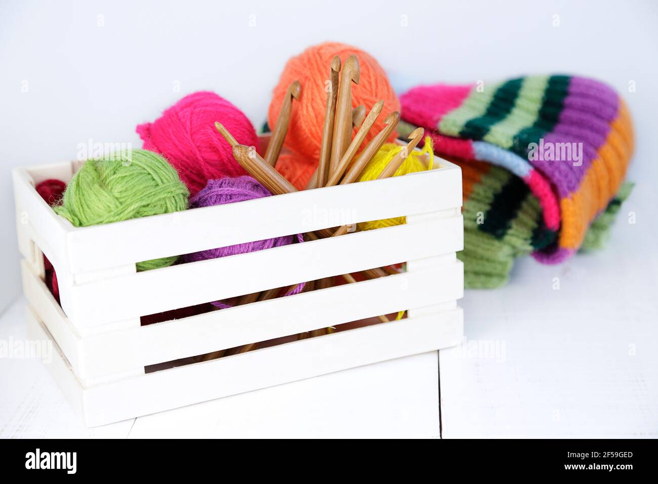 Boîte en bois avec crochets en crochet de bambou naturel et boules de laine de différentes couleurs. Banque D'Images