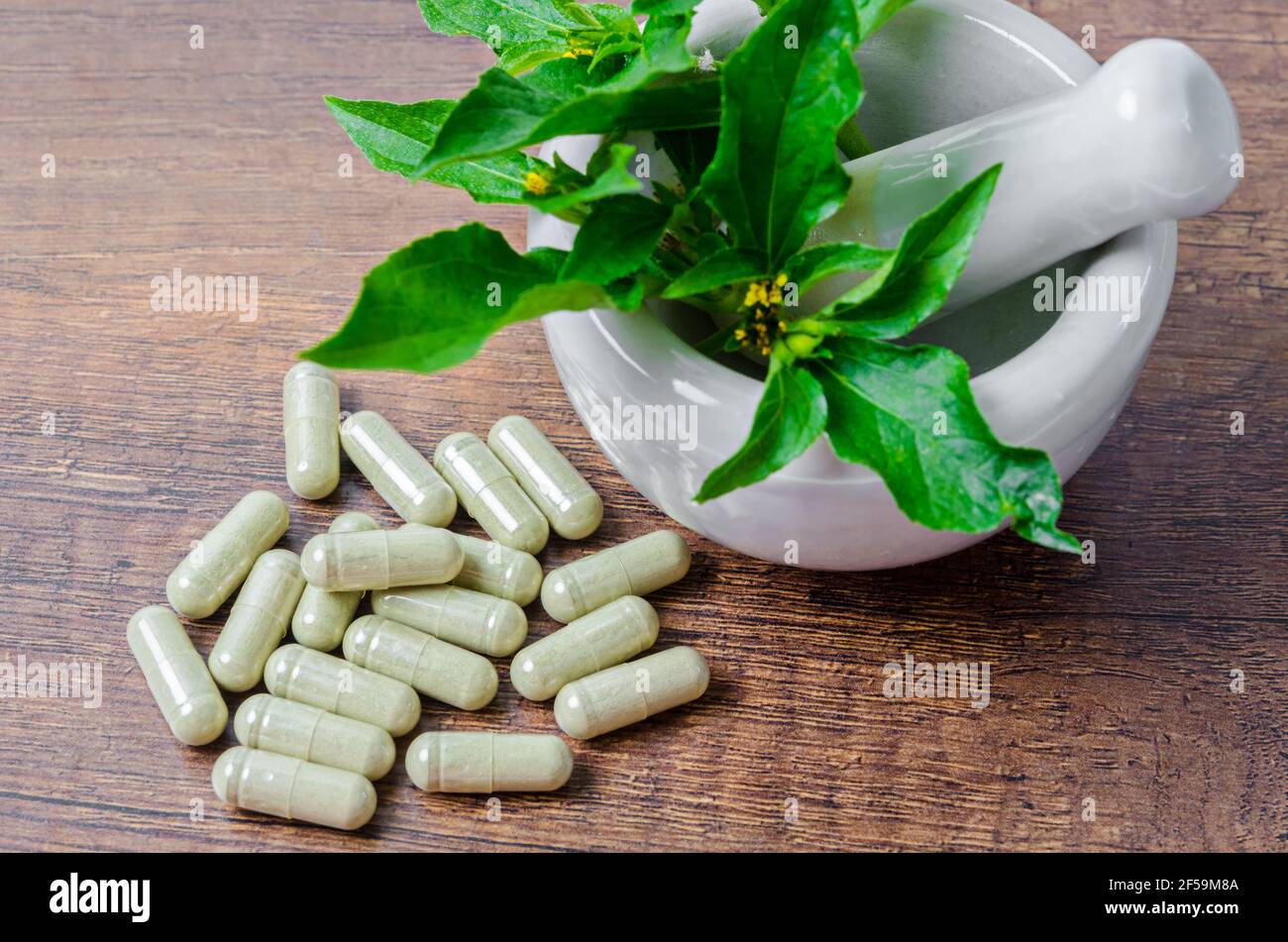 Pile de plantes médicinales en capsules et mortier céramique avec feuille verte sur fond de bois. Banque D'Images