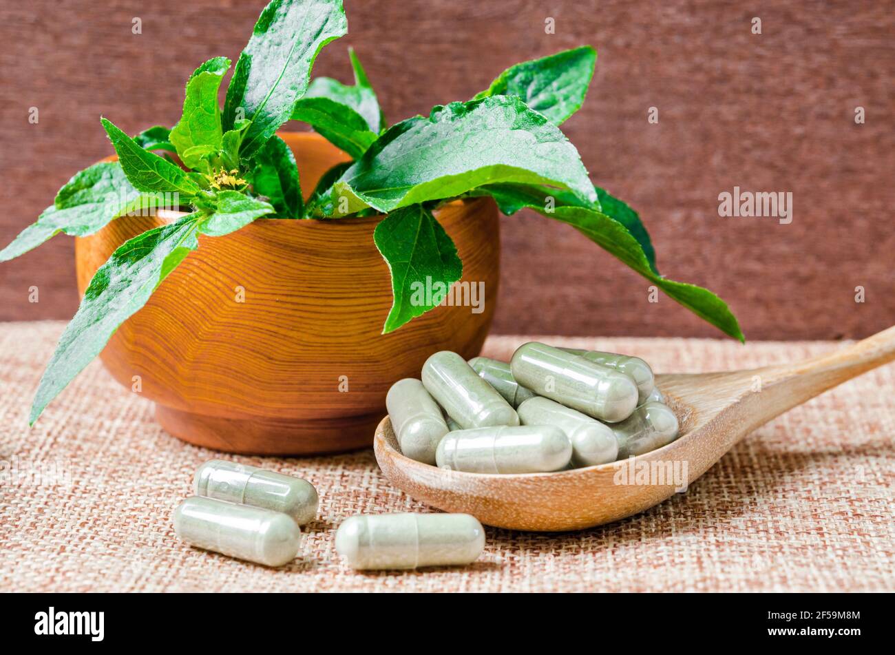 Pile de capsules de phytothérapie dans une cuillère en bois avec une feuille verte sur fond de sac. Banque D'Images