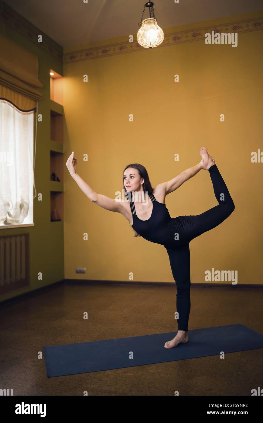 Femme attirante en noir pleine longueur vêtements de sport pratiquant le yoga en studio exécutant l'exercice natarajasana, roi des danseurs pose. Banque D'Images