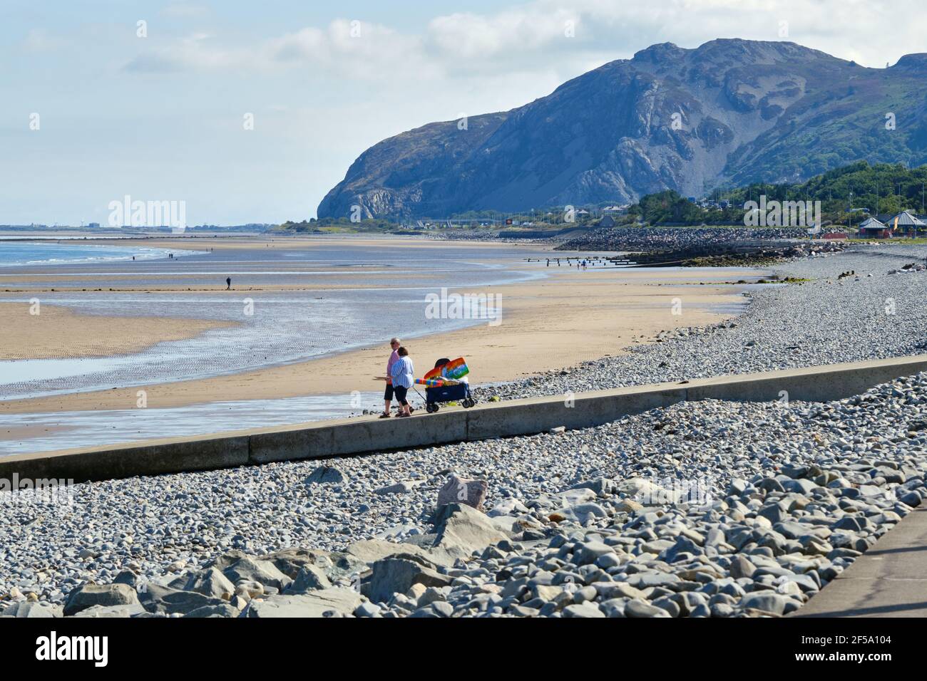 Un couple se dirige vers la plage avec un chariot chargé de fournitures pour une journée au bord de la mer. Banque D'Images