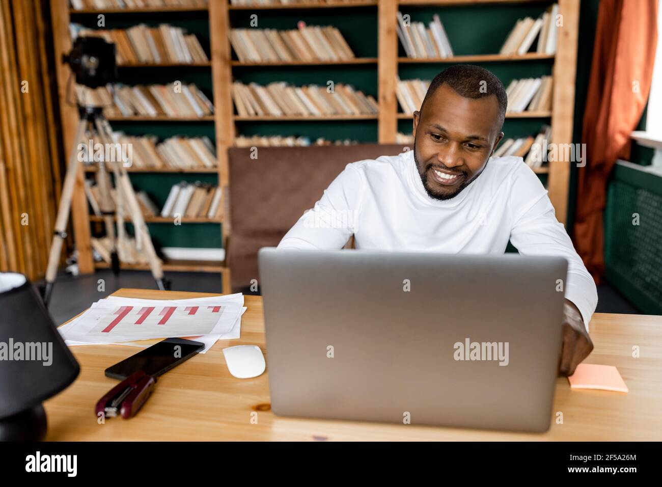Un employé ou un étudiant heureux a une réunion vidéo avec des amis ou des collègues, souriant. Joyeux jeune homme d'affaires adulte travaille de chez lui Banque D'Images
