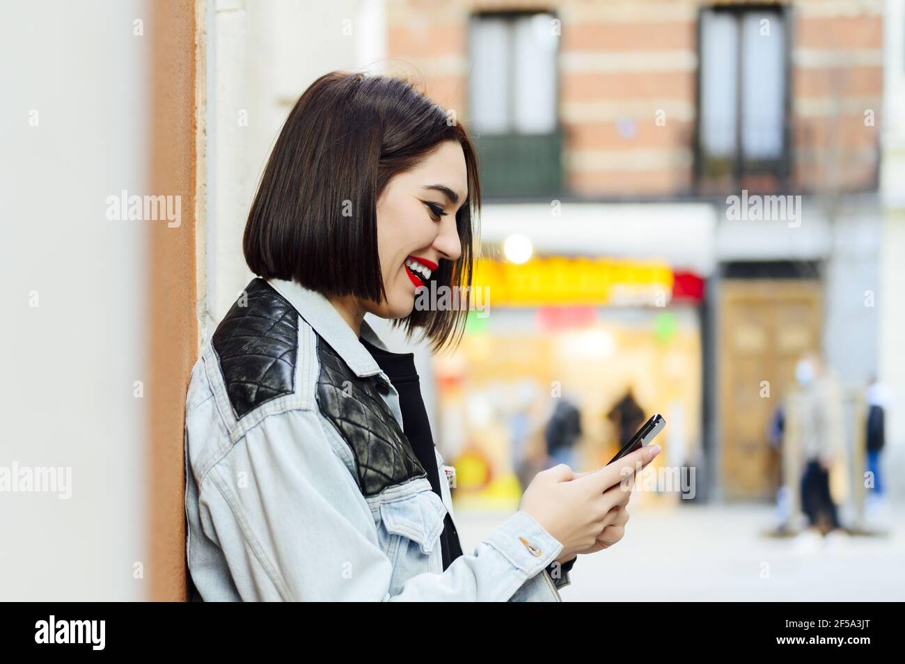 Bonne fille espagnole portant une coupe de style bob et élégante votre tenue envoie des sms sur votre smartphone Banque D'Images