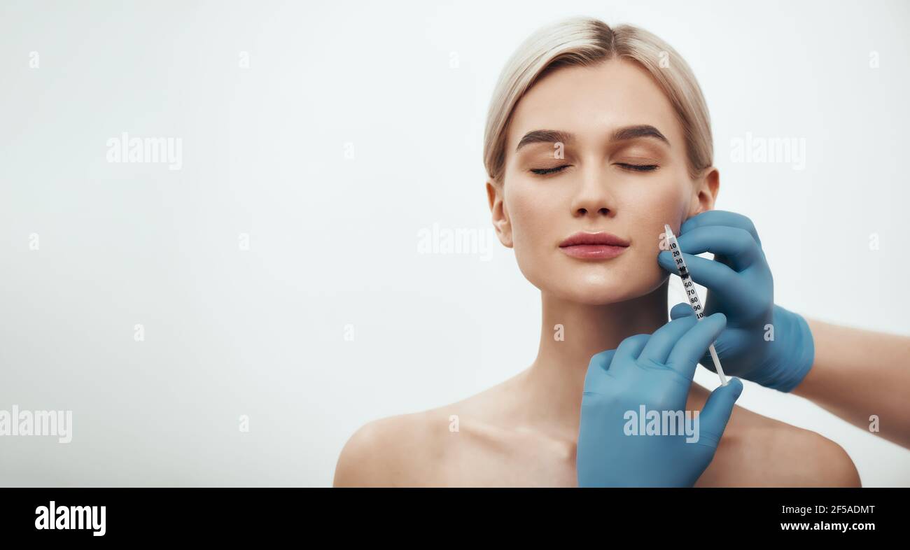 Jeune jolie femme gardant les yeux fermés tandis que les médecins font une injection dans son visage. Bannière Web horizontale. Banque D'Images