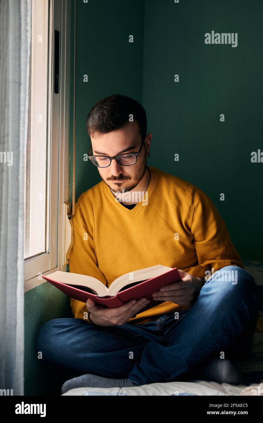 Un jeune homme lit un livre à côté de sa chambre fenêtre Banque D'Images