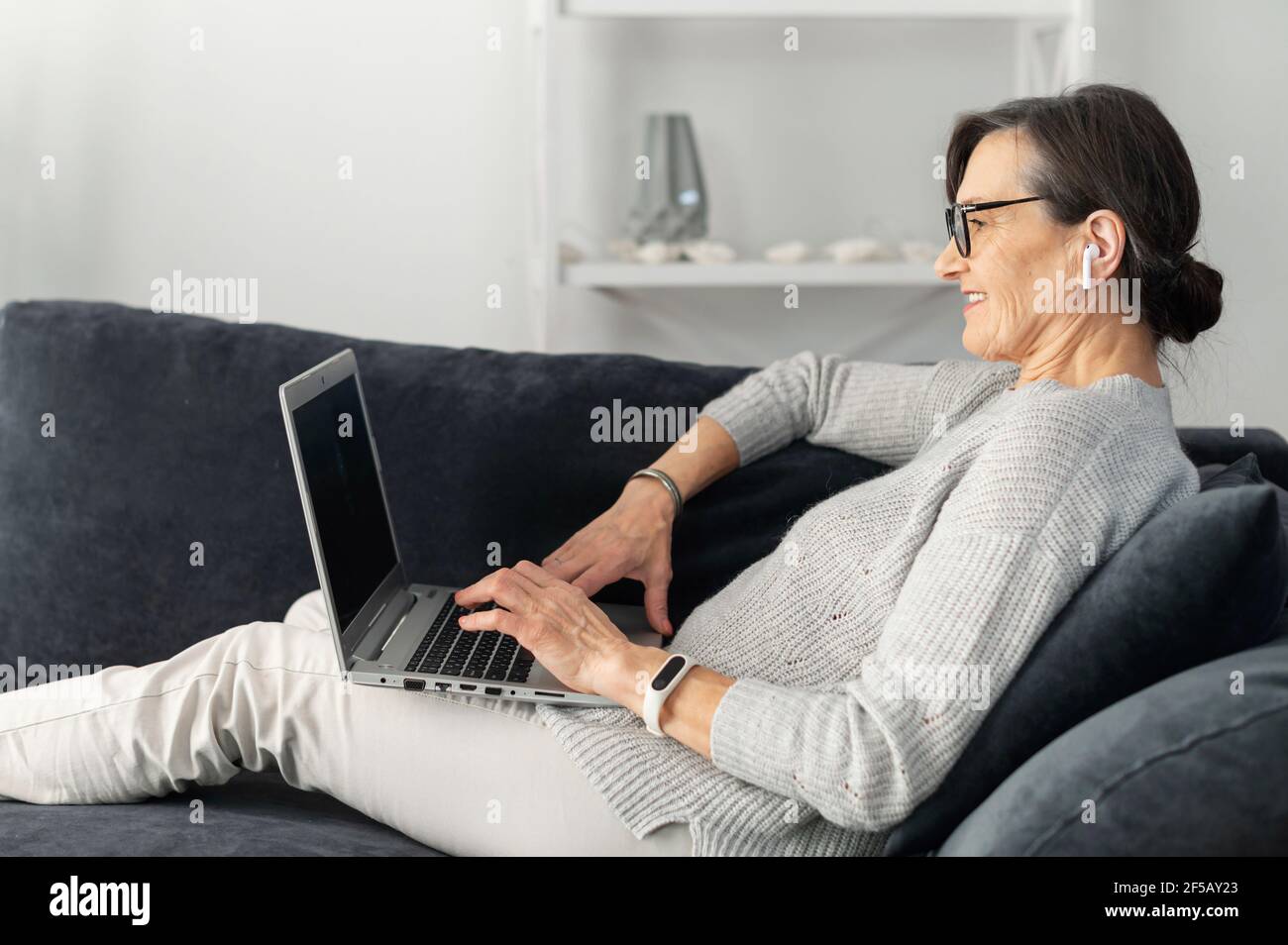 La femme contemporaine aime bavarder sur les réseaux sociaux, se coucher sur le confortable canapé avec un ordinateur portable, passer du temps libre sur le réseau, envoyer des SMS par e-mail, se connecter avec des amis à distance Banque D'Images