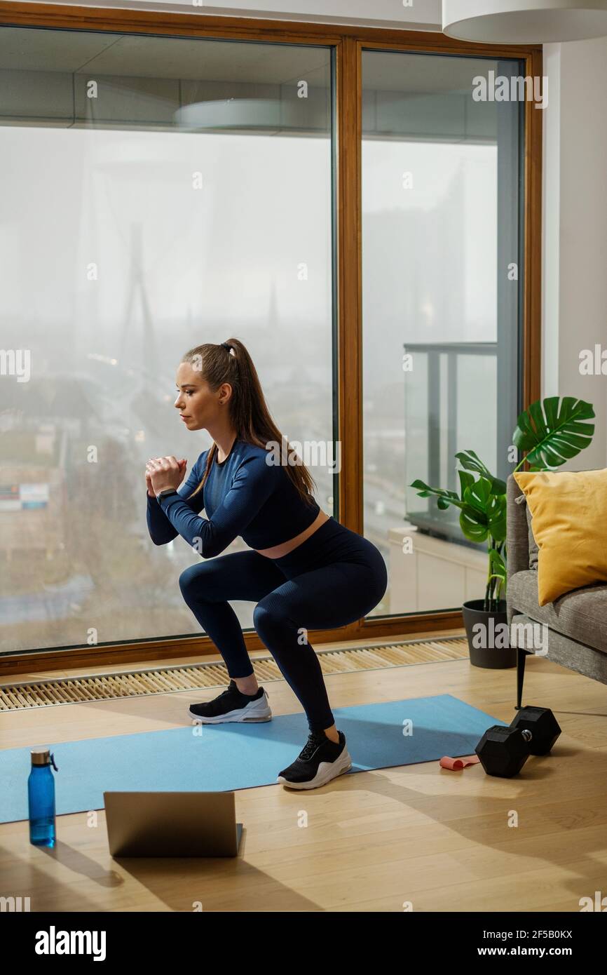 Femme en survêtement en position de squat par fenêtre panoramique Banque D'Images