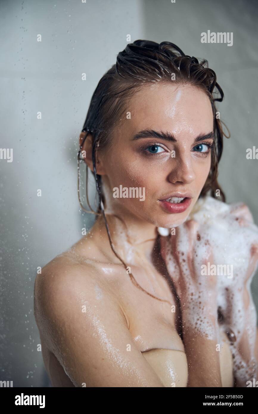 Jeune femme avec une éponge de bain savonnante qui regarde devant vous Banque D'Images