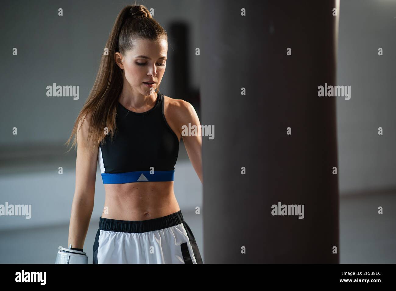 Portrait d'un boxeur jeune fille attrayant dans la salle de gym portant des gants à côté d'un sac de poinçonnage. Banque D'Images